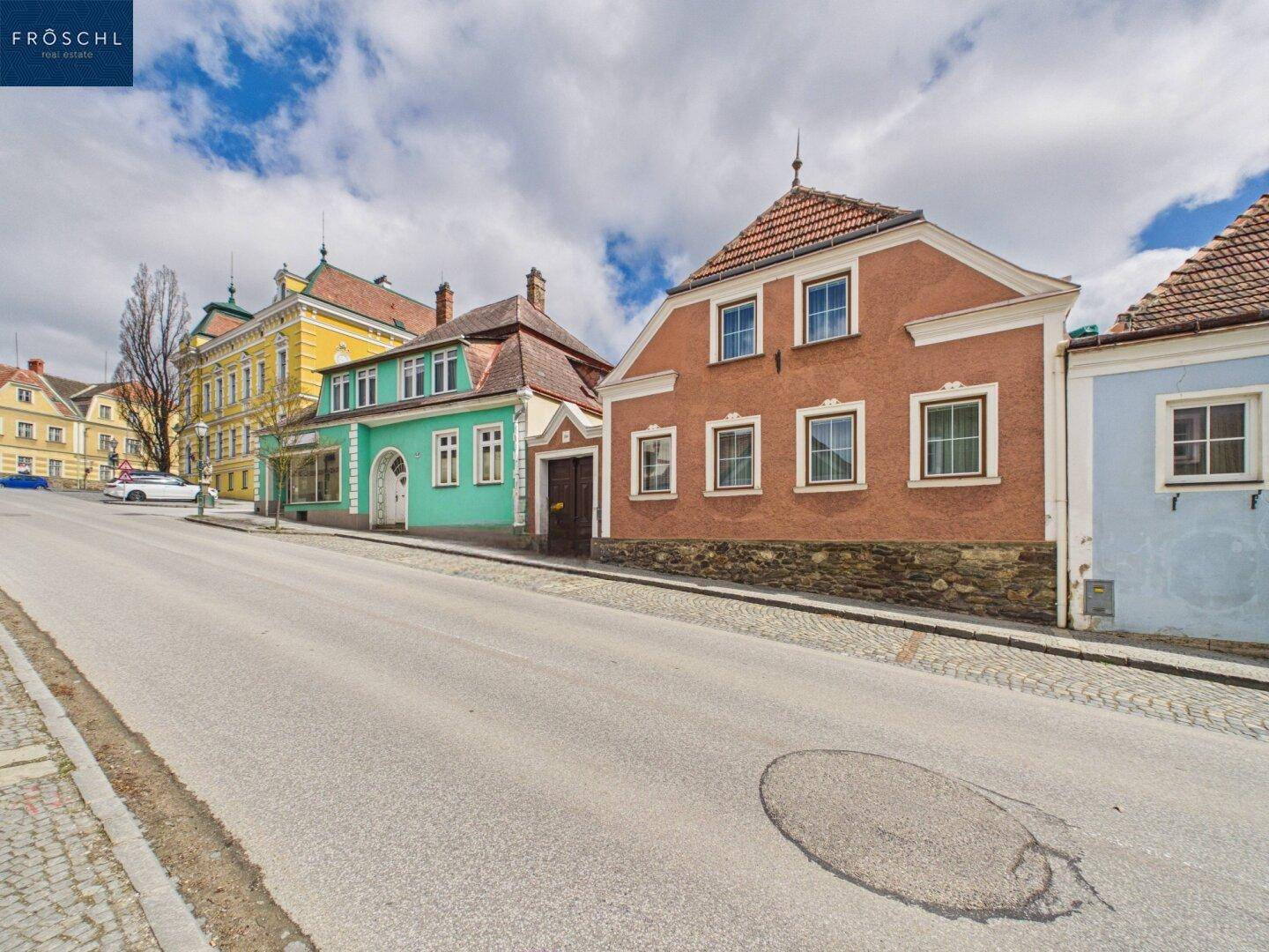 Historische Gebäudezeile mit farbigen Fassaden entlang einer gepflasterten Straße.
