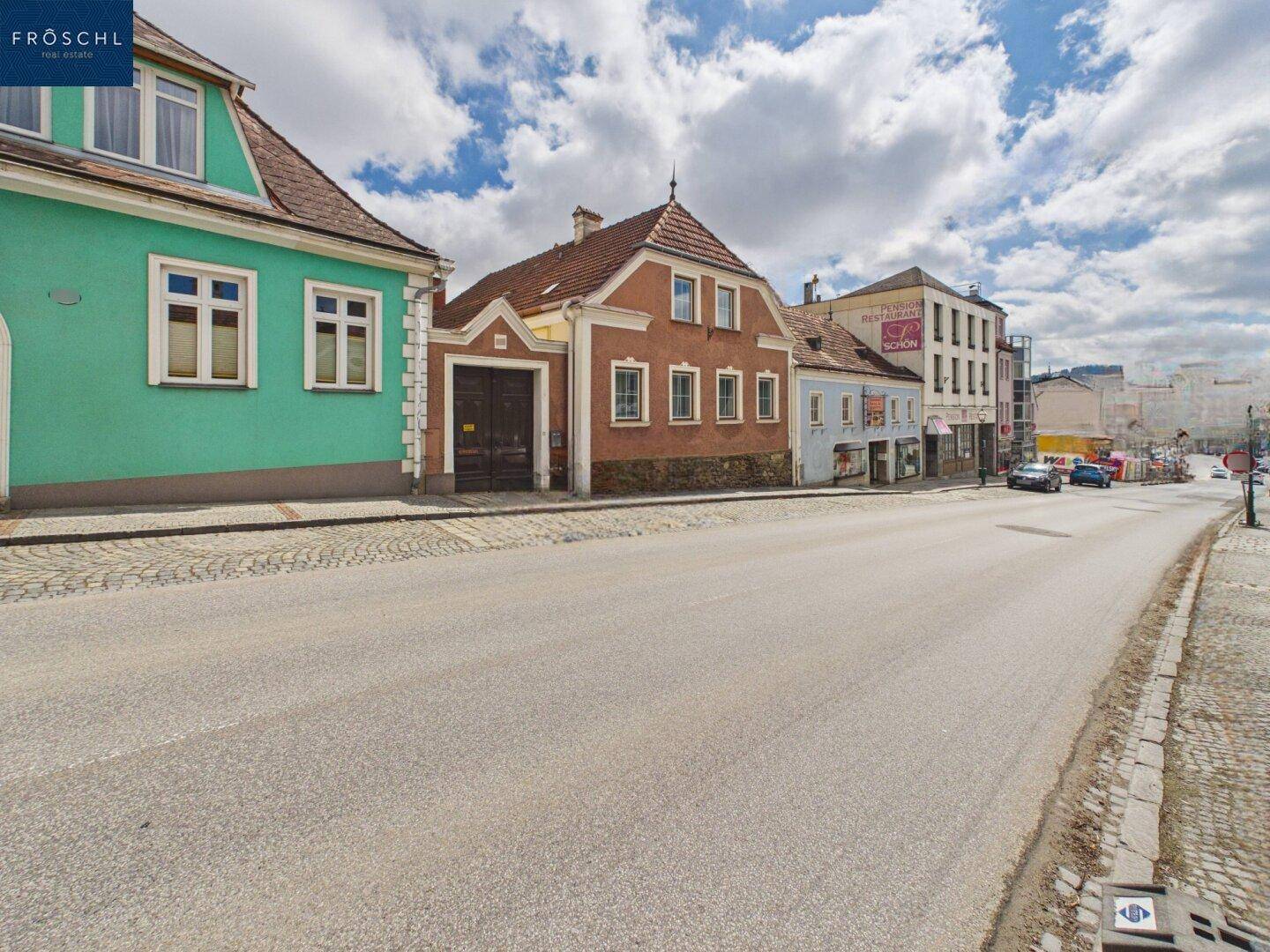 Stadtansicht mit historischen Gebäuden und einer belebten Straße unter bewölktem Himmel.