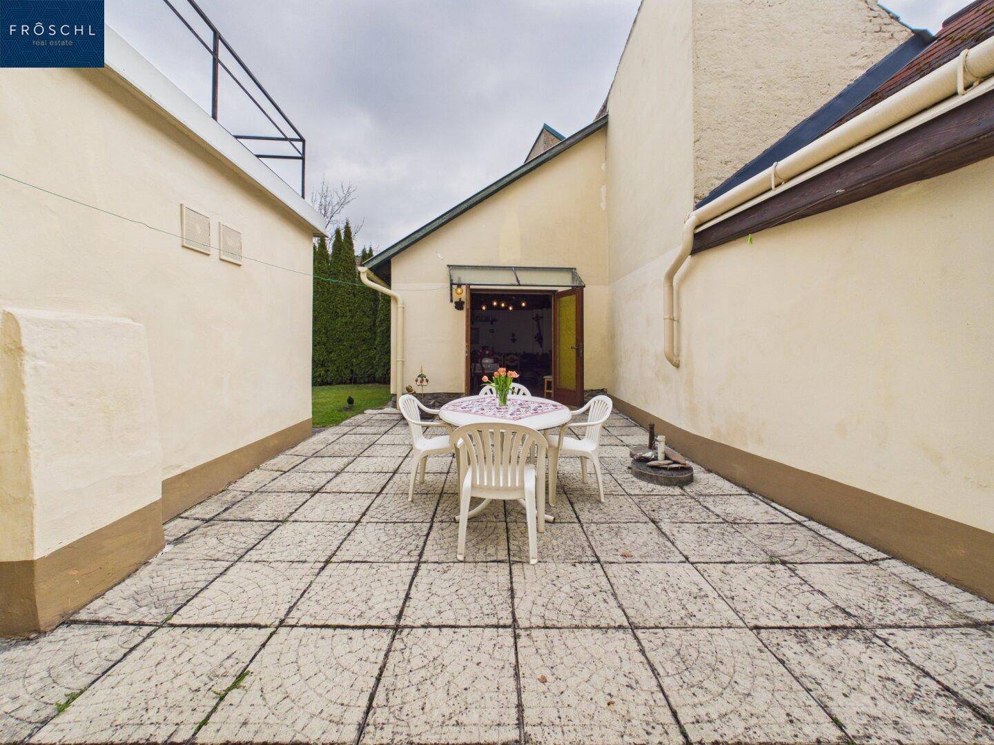 Gepflasterte Terrasse mit Gartenmöbeln, umgeben von hohen Mauern und Grünflächen.