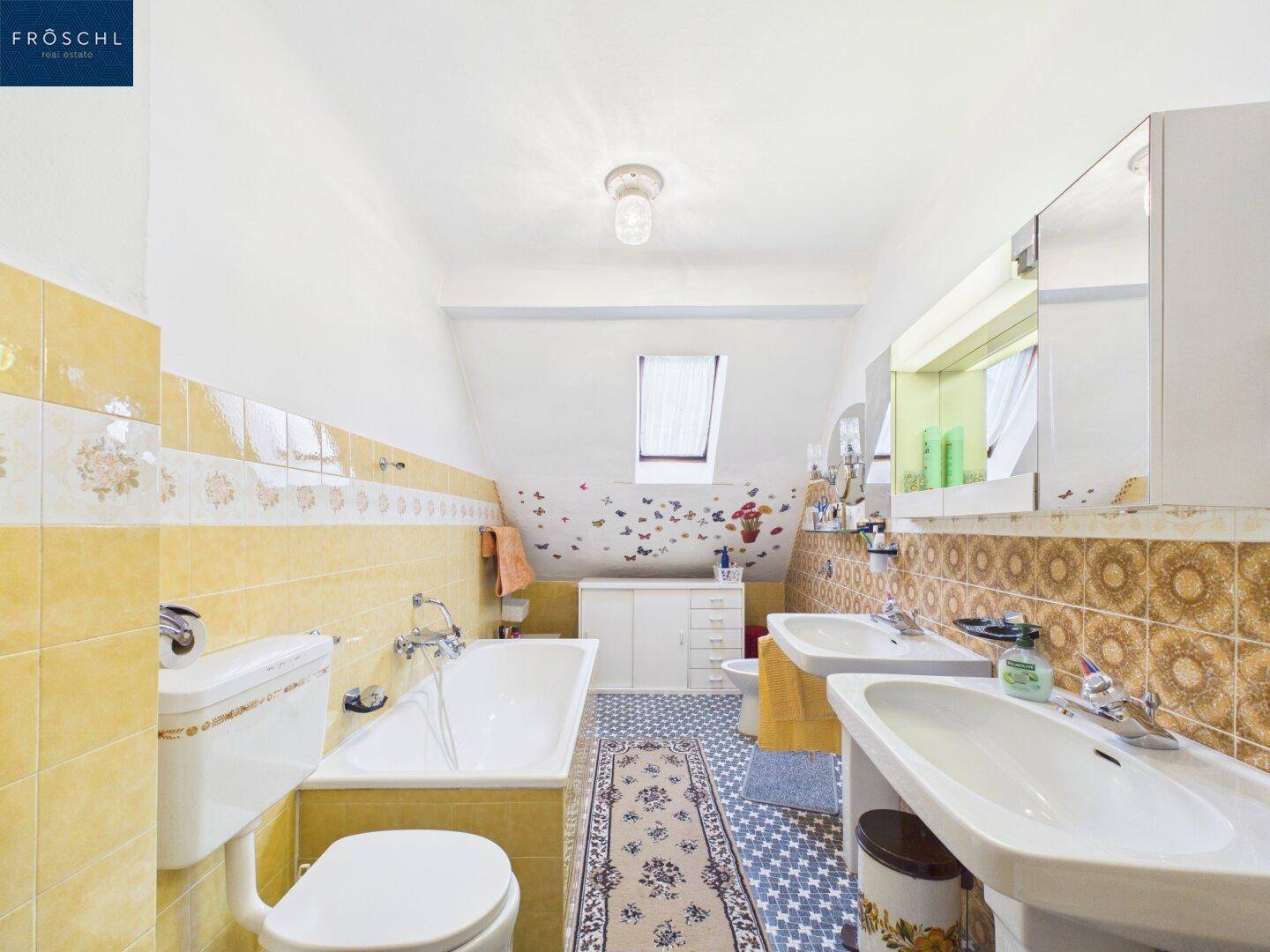 Badezimmer mit gelben Fliesen, Badewanne, Doppelwaschbecken und Dachfenster.