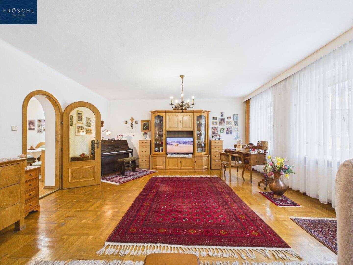 Helles Wohnzimmer mit Parkettboden, traditionellen Holzmöbeln und großen Fenstern.