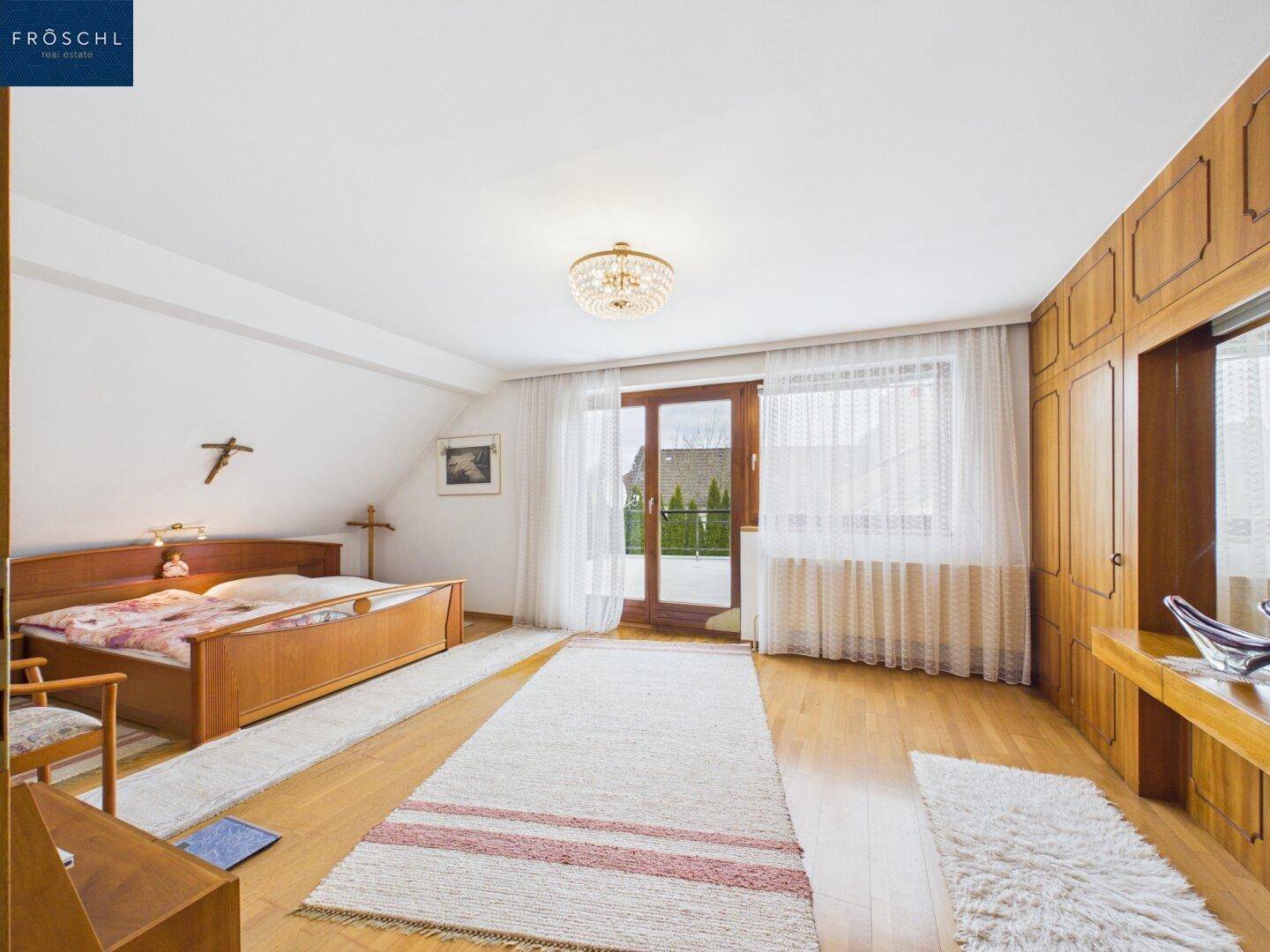 Helles Schlafzimmer mit Holzbett, Parkettboden und Zugang zu einem Balkon oder einer Terrasse.