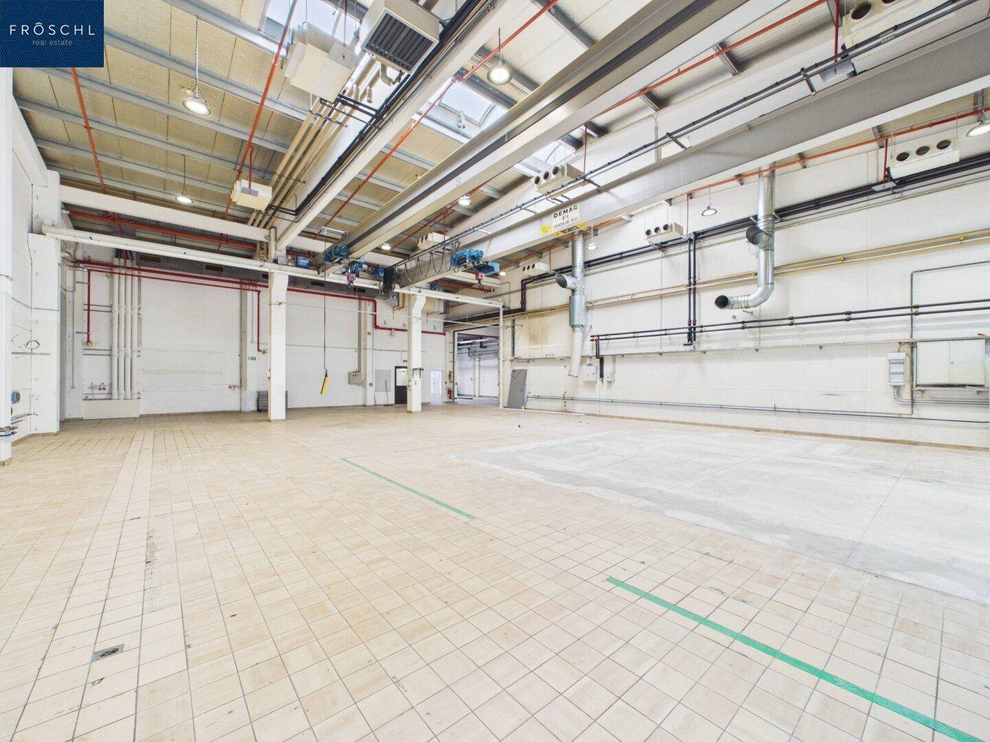 Industriehalle mit Fliesenboden, hohen Decken und sichtbaren Installationen, bereit zur Nutzung.