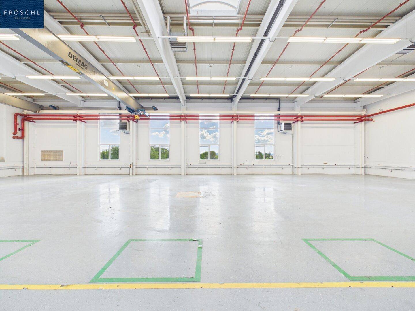 Weitläufige Industriehalle mit Betonboden, hohen Decken und großen Fenstern, bereit zur Nutzung und gut beleuchtet.