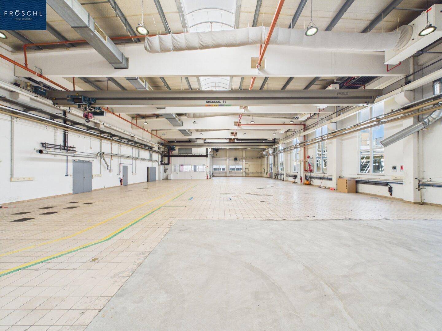 Geräumige Halle mit einer Kombination aus Fliesen- und Betonboden, hohen Decken und Oberlichtern.
