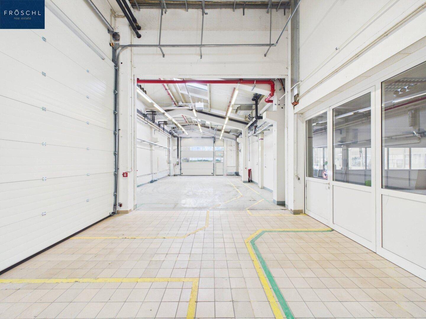 Innenansicht einer Laderampe mit Rolltor, die in eine große, helle Industriehalle führt.