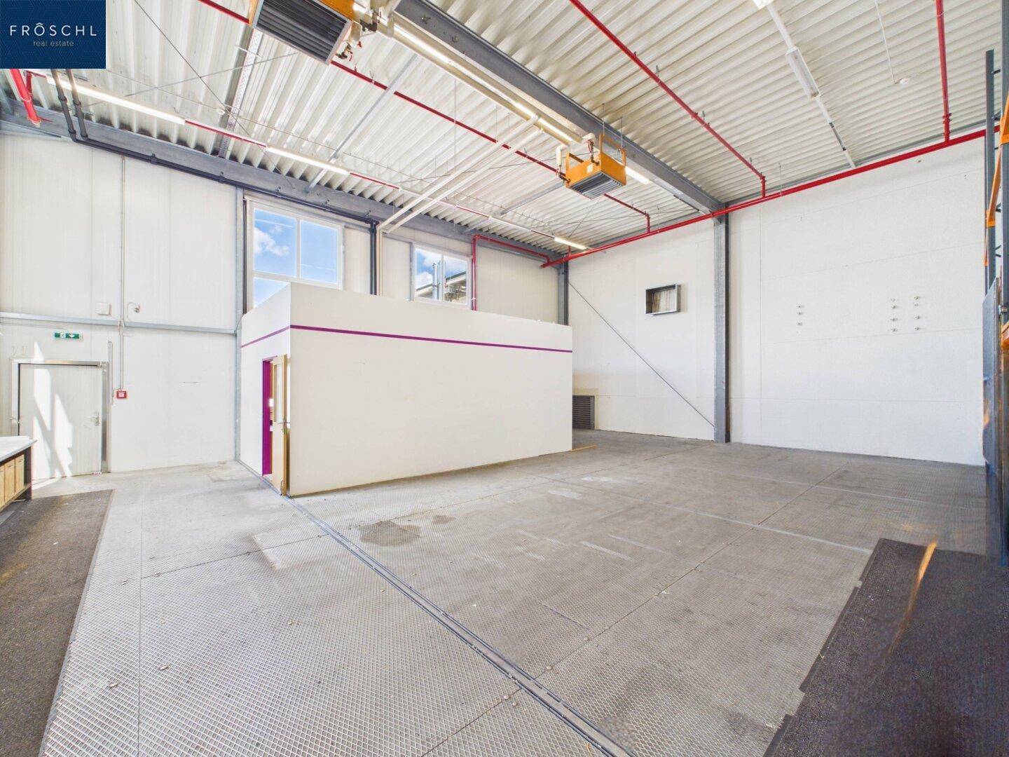 Geräumige Industriehalle mit Betonboden und einer kleinen, freistehenden Büro- oder Lagerbox.