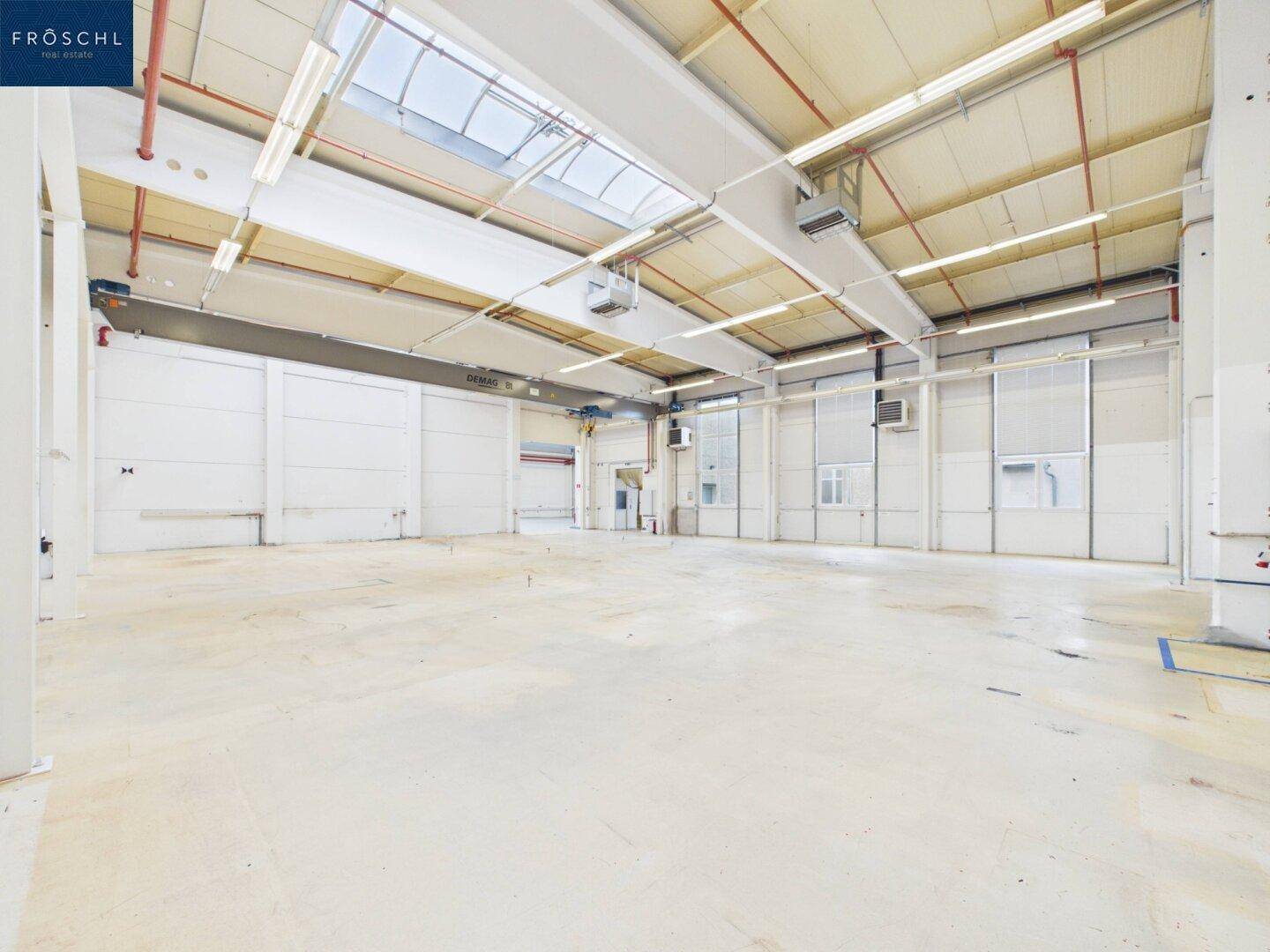 Weitläufige Industriehalle mit hellem Betonboden, hohen Decken und Oberlichtern für natürliches Licht.
