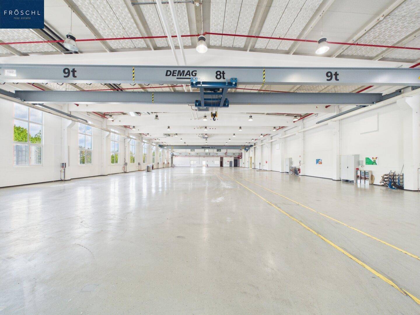 Weitläufige Industriehalle mit mehreren Kränen, hohen Decken und glänzendem Betonboden.