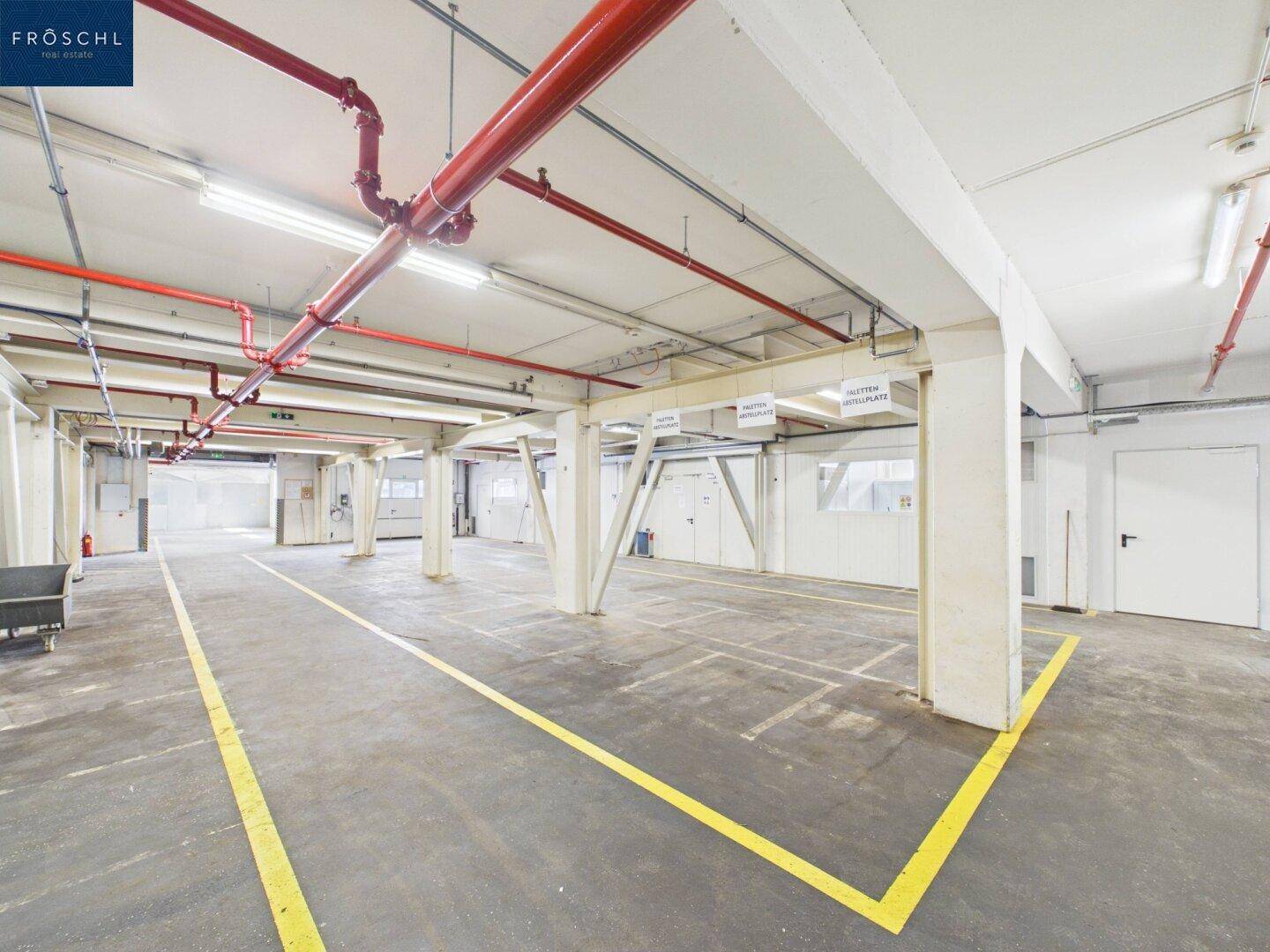 Geräumiger Industriebereich mit Betonboden, gelben Markierungen und sichtbaren roten Rohrleitungen.