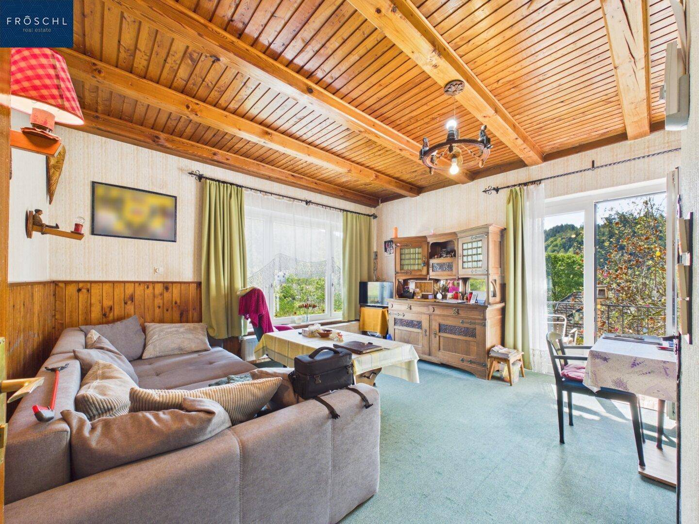 Gemütliches Wohnzimmer mit Holzbalkendecke, Sofa und Blick ins Grüne.