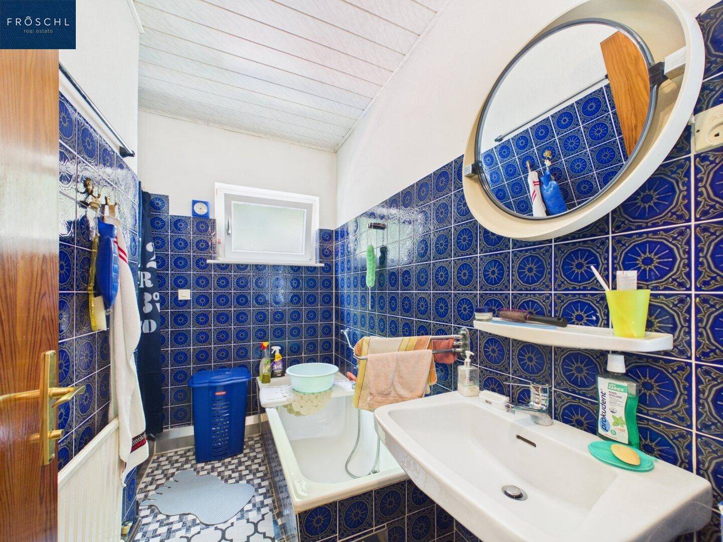 Badezimmer mit blauen Fliesen, Badewanne und einem Fenster für Tageslicht.
