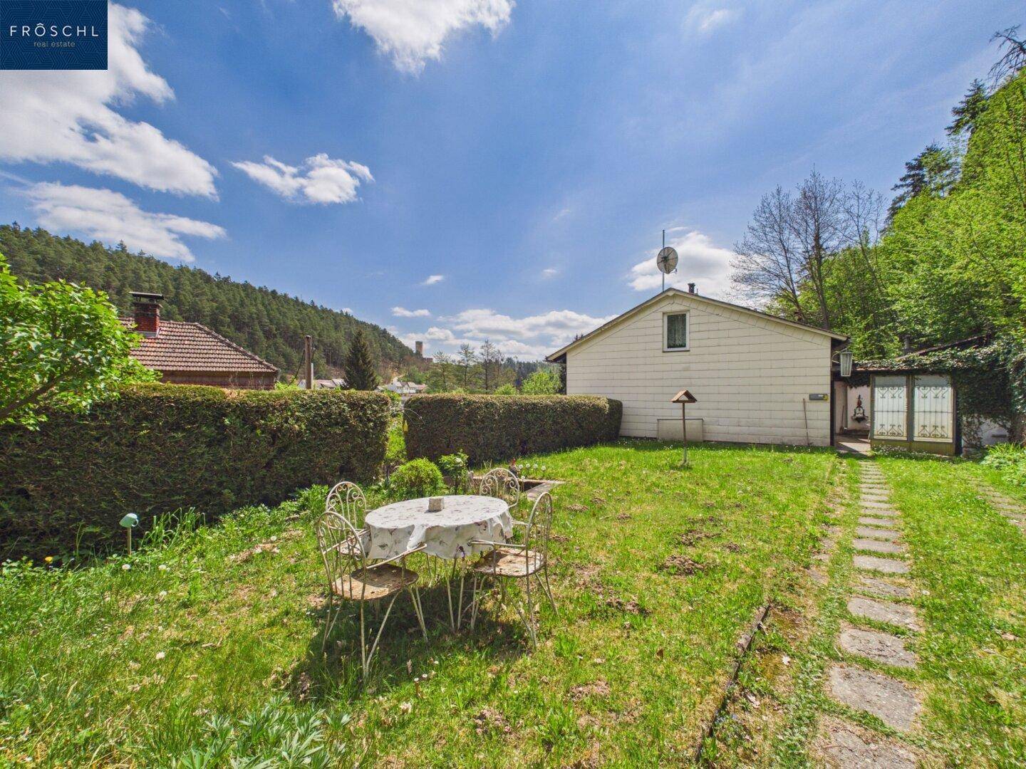 Großer Gartenbereich mit Rasenfläche, Hecke und einem kleinen Sitzplatz.