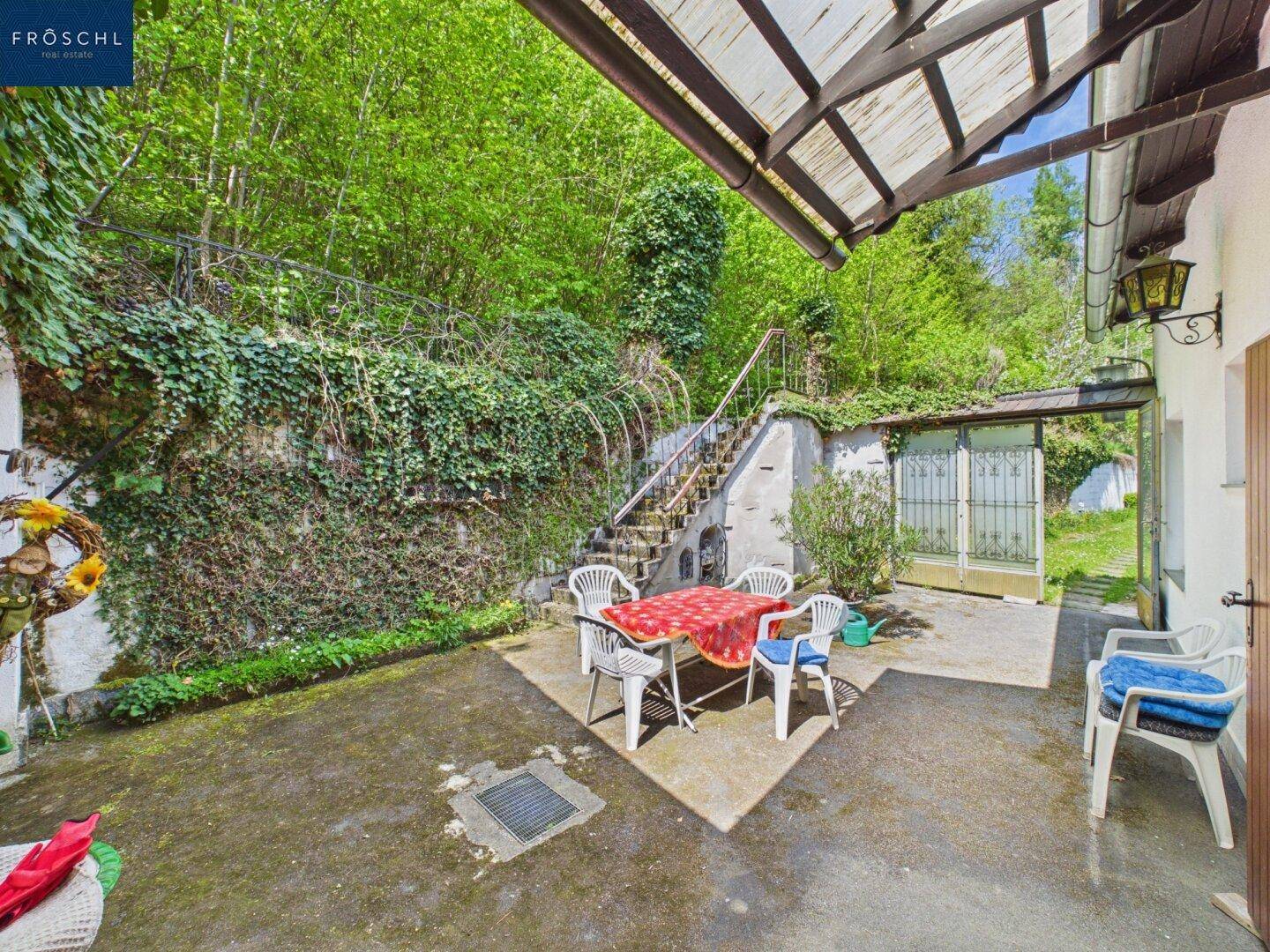 Gemütliche Terrasse mit Sitzgruppe und üppiger Vegetation im Hintergrund.