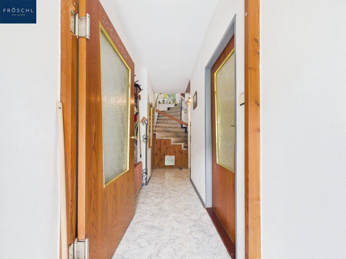 Schmaler Flur mit Holztüren und Treppenaufgang in die obere Etage.
