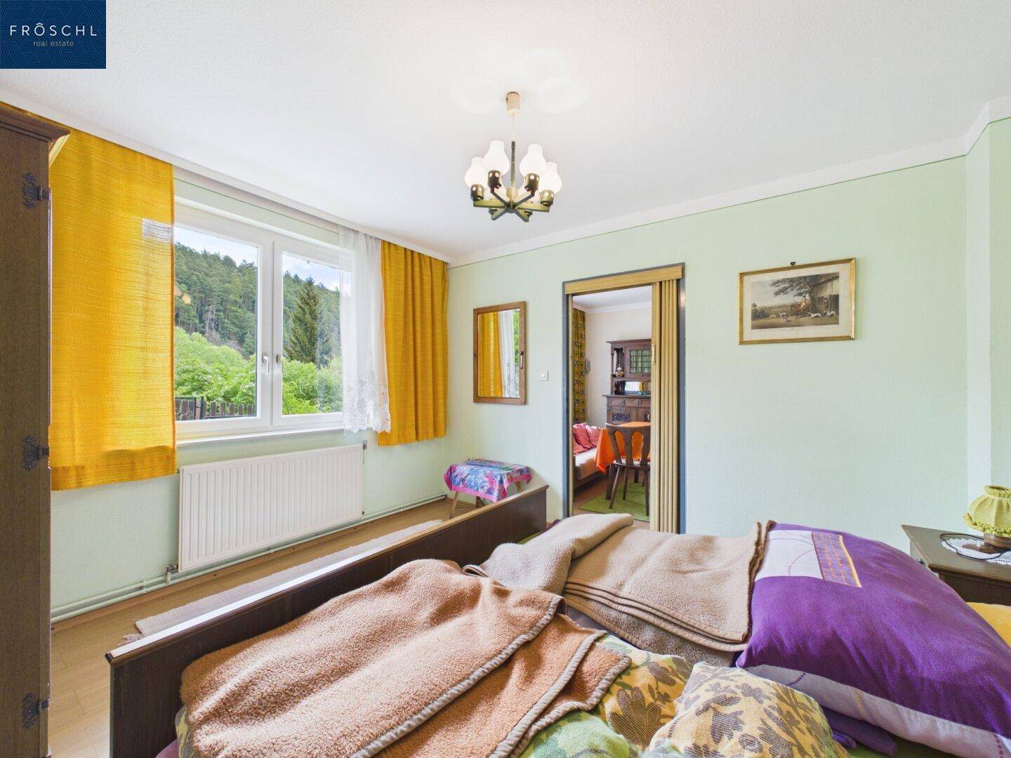 Schlafzimmer mit Einzelbett, Fenster und Blick auf die grüne Umgebung.