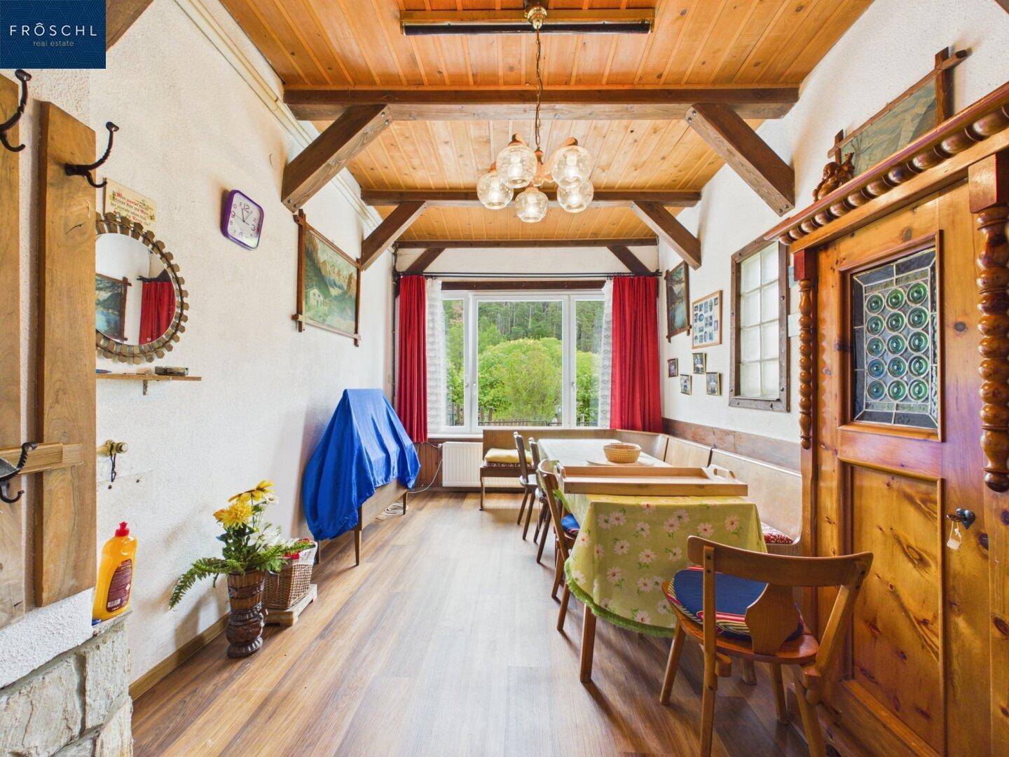 Geräumiger Essbereich mit Holzbalkendecke, großer Sitzbank und Blick ins Grüne.