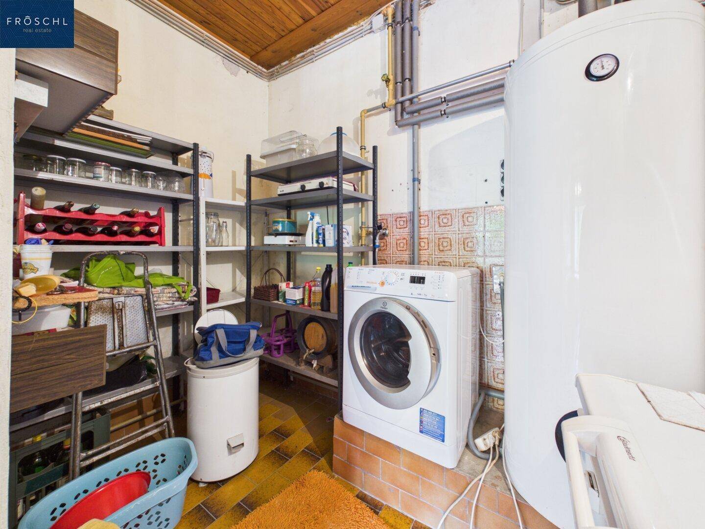 Hauswirtschaftsraum mit Waschmaschine, Regalen und Warmwasserboiler.