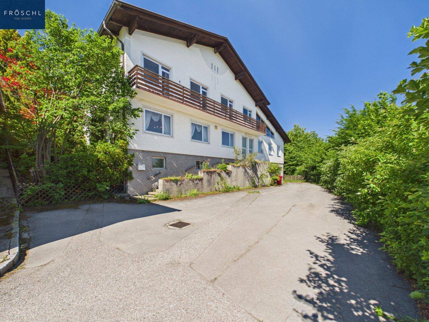 Mehrstöckiges Wohnhaus mit Balkonen und umgebender Vegetation an einem sonnigen Tag.