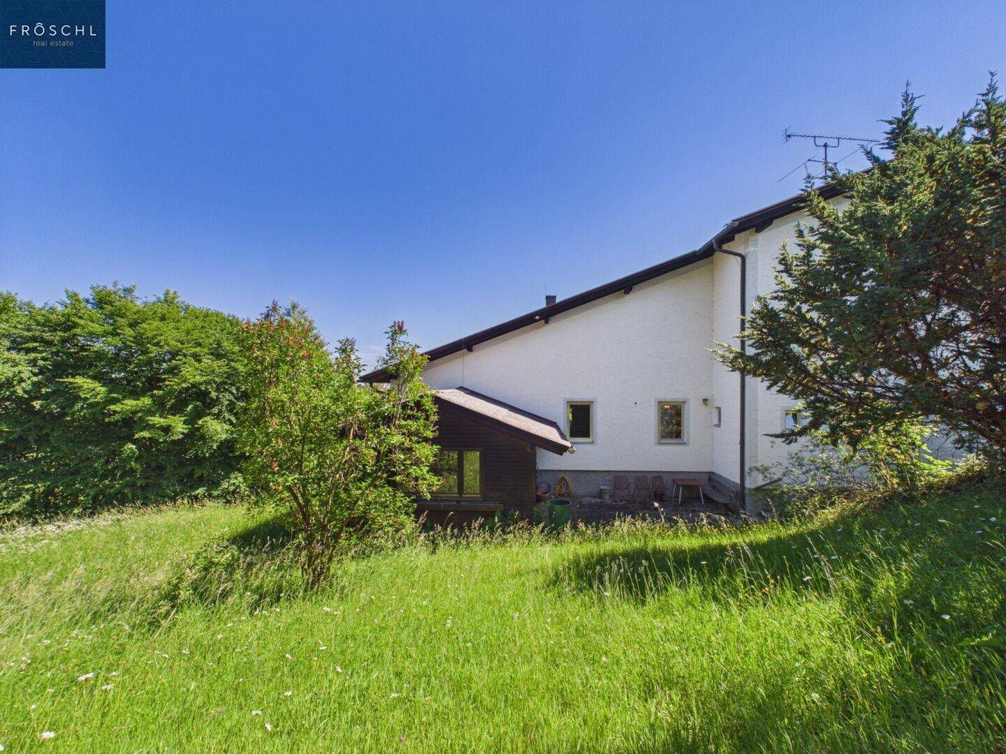 Seitenansicht des Hauses mit großem Rasenbereich und umgebender Natur.