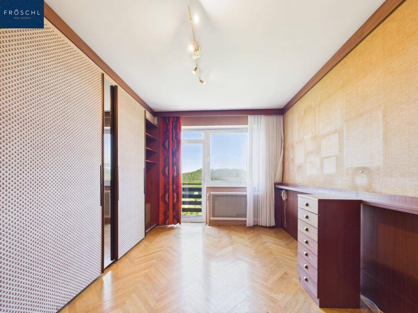 Schlafzimmer mit Parkettboden, Einbauschränken und Zugang zum Balkon.