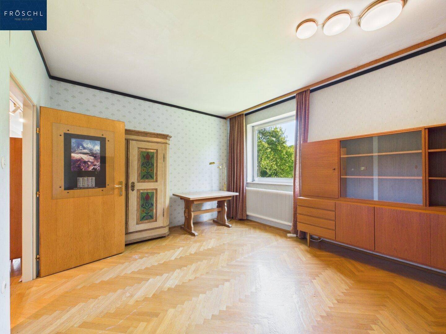 Schlafzimmer mit Parkettboden, traditionellen Möbeln und Fensterblick ins Grüne.