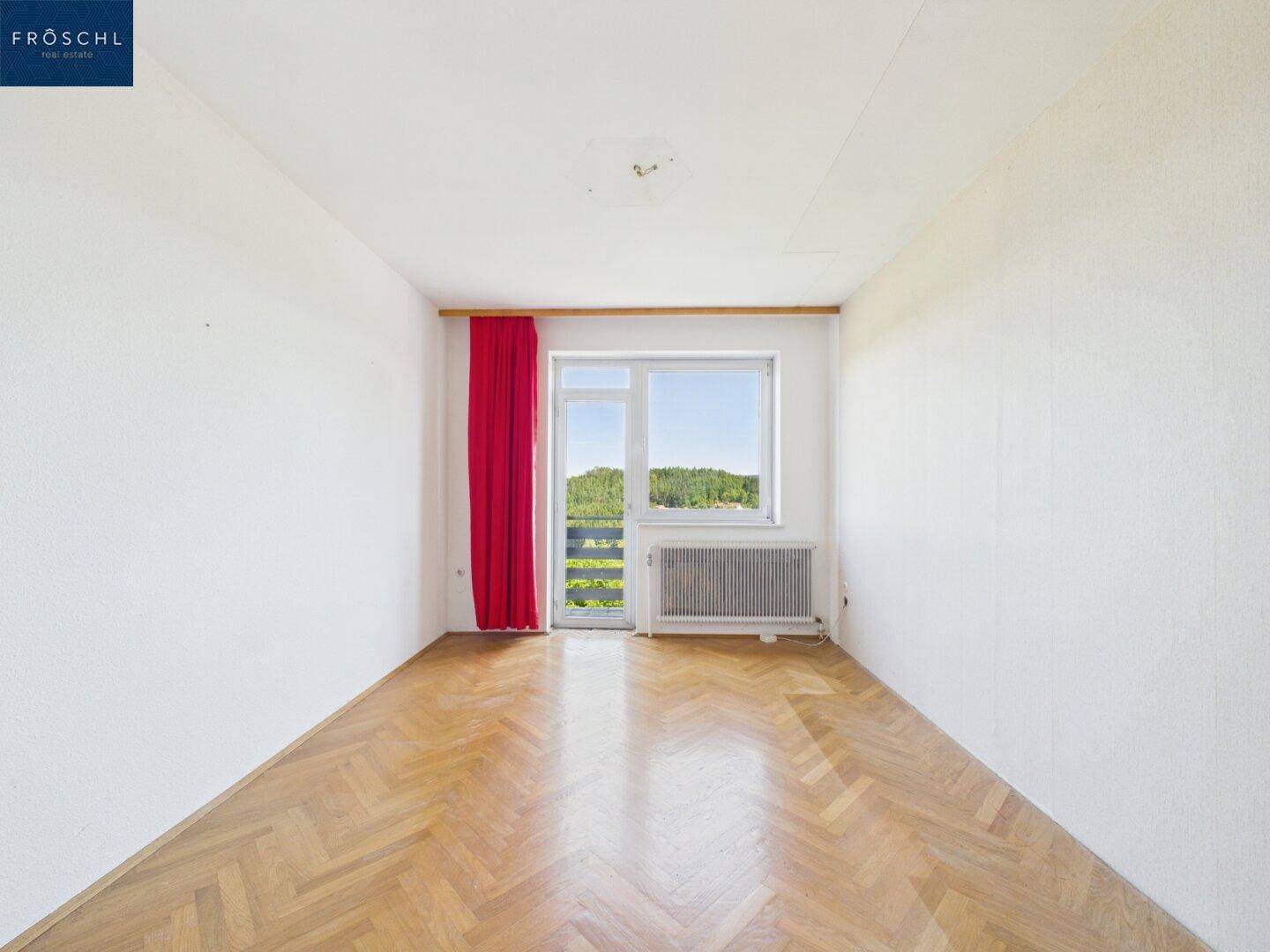 Helles Schlafzimmer mit Parkettboden, weißen Wänden und Balkonzugang.