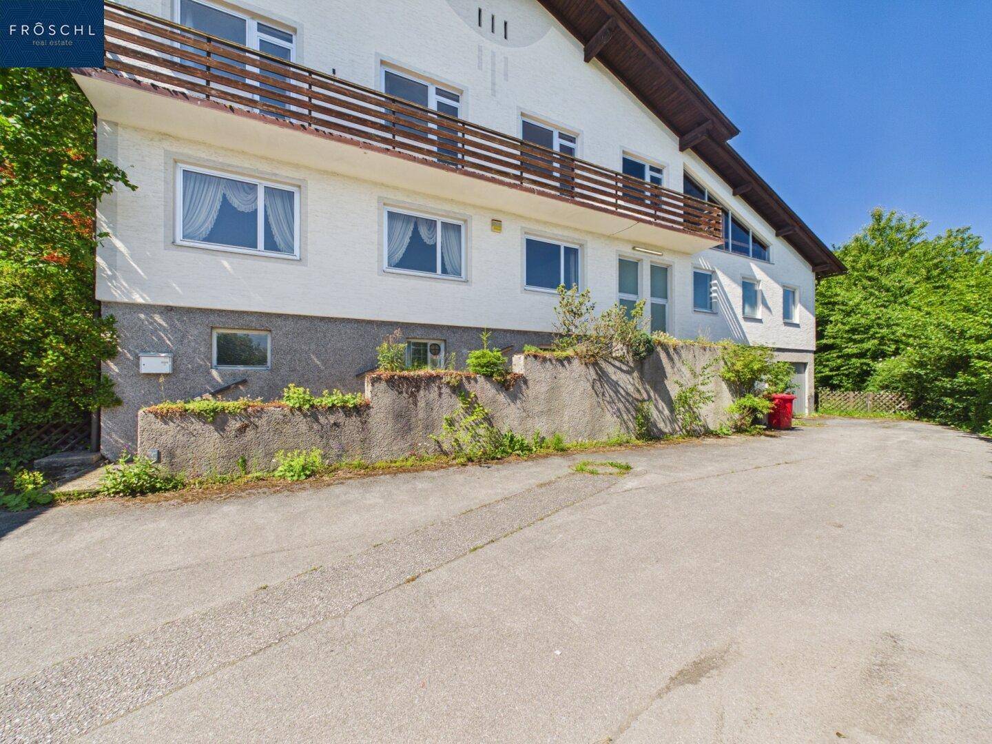 Mehrstöckiges Gebäude mit Balkon, weißer Fassade und Zufahrt im Vordergrund.