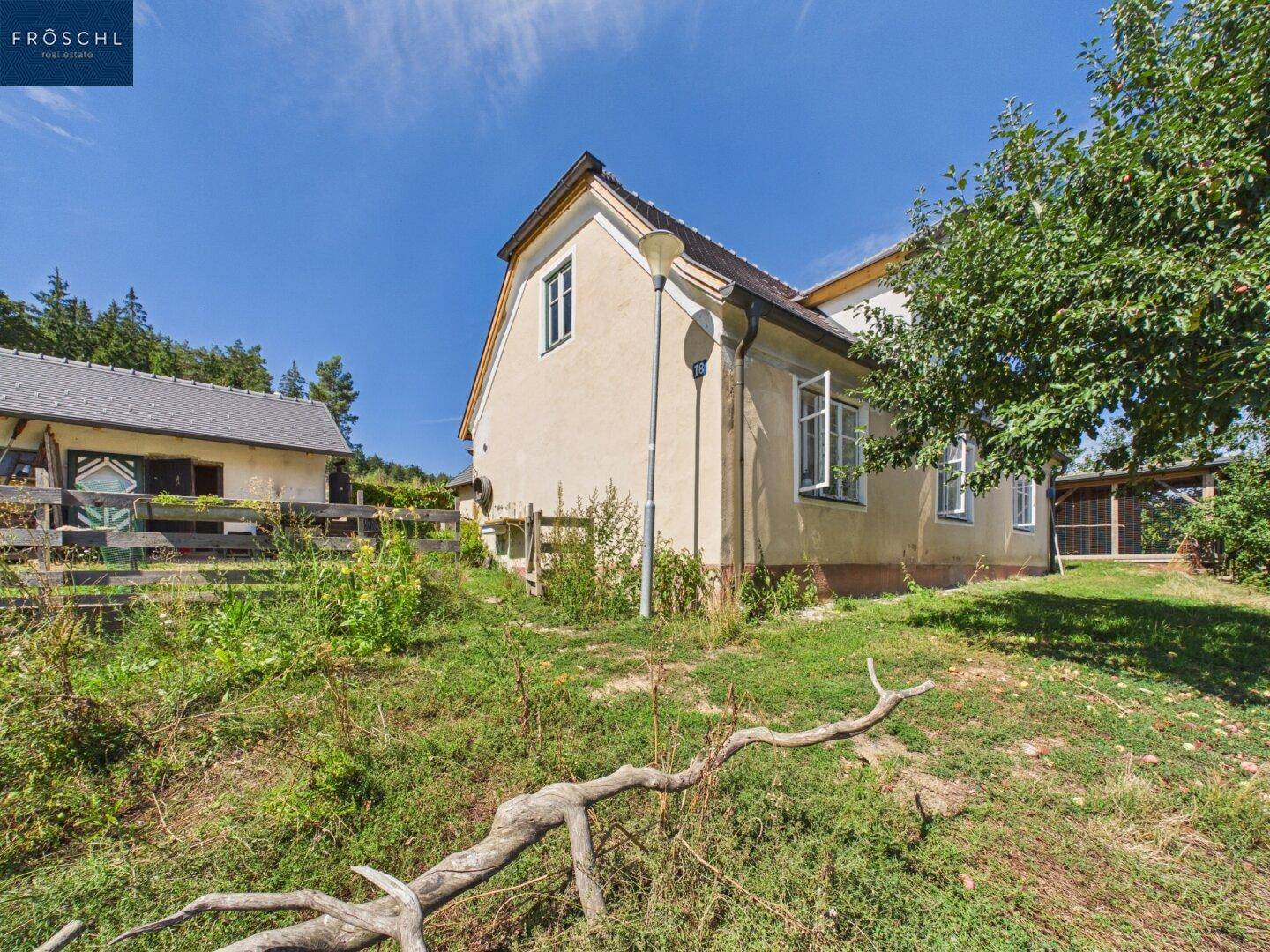 Seitenansicht eines ländlichen Hauses mit Fenstern und einem Gartenbereich unter blauem Himmel.