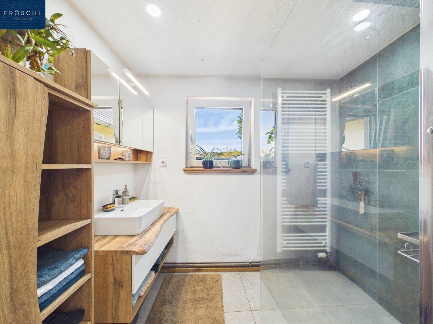 Modernes Badezimmer mit großformatigen Fliesen, begehbarer Dusche und Fenster.
