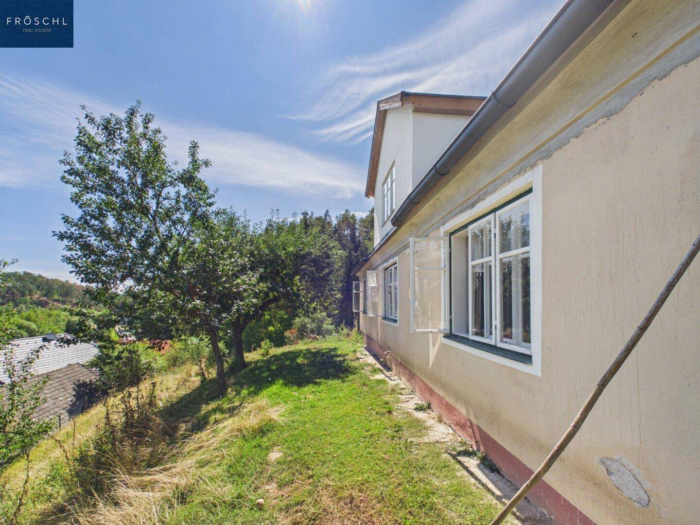 Seitenansicht des Hauses mit Fenstern und sonnigem Gartenbereich.