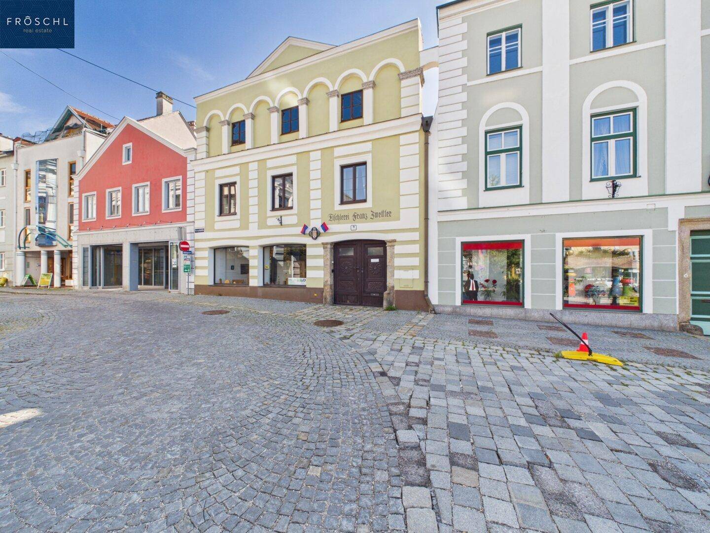 Historische Gebäudezeile an einer gepflasterten Straße mit Schaufenstern und traditioneller Architektur.
