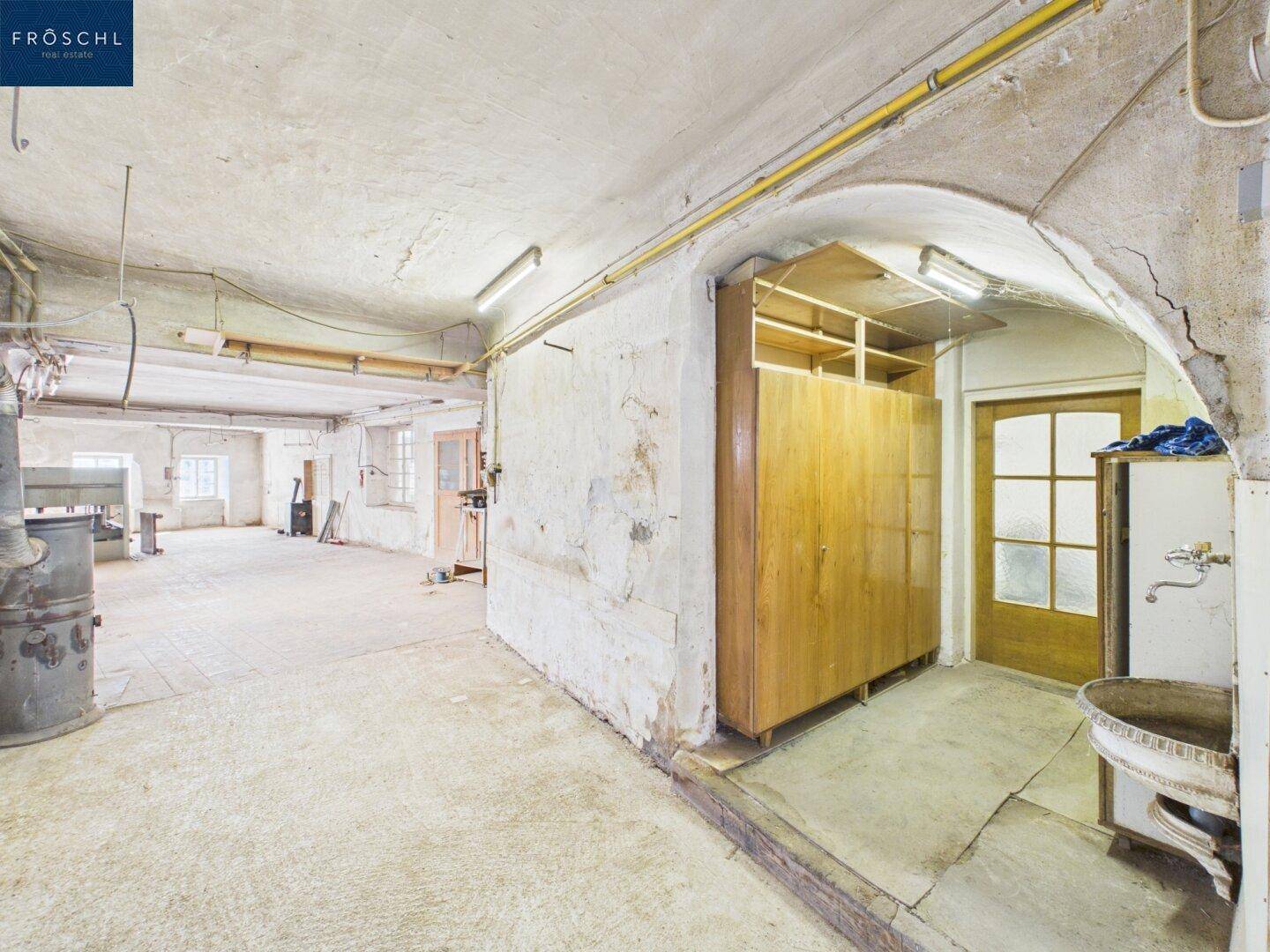 Großer Kellerraum mit rauen Wänden, Betonboden und einem alten Waschbecken.