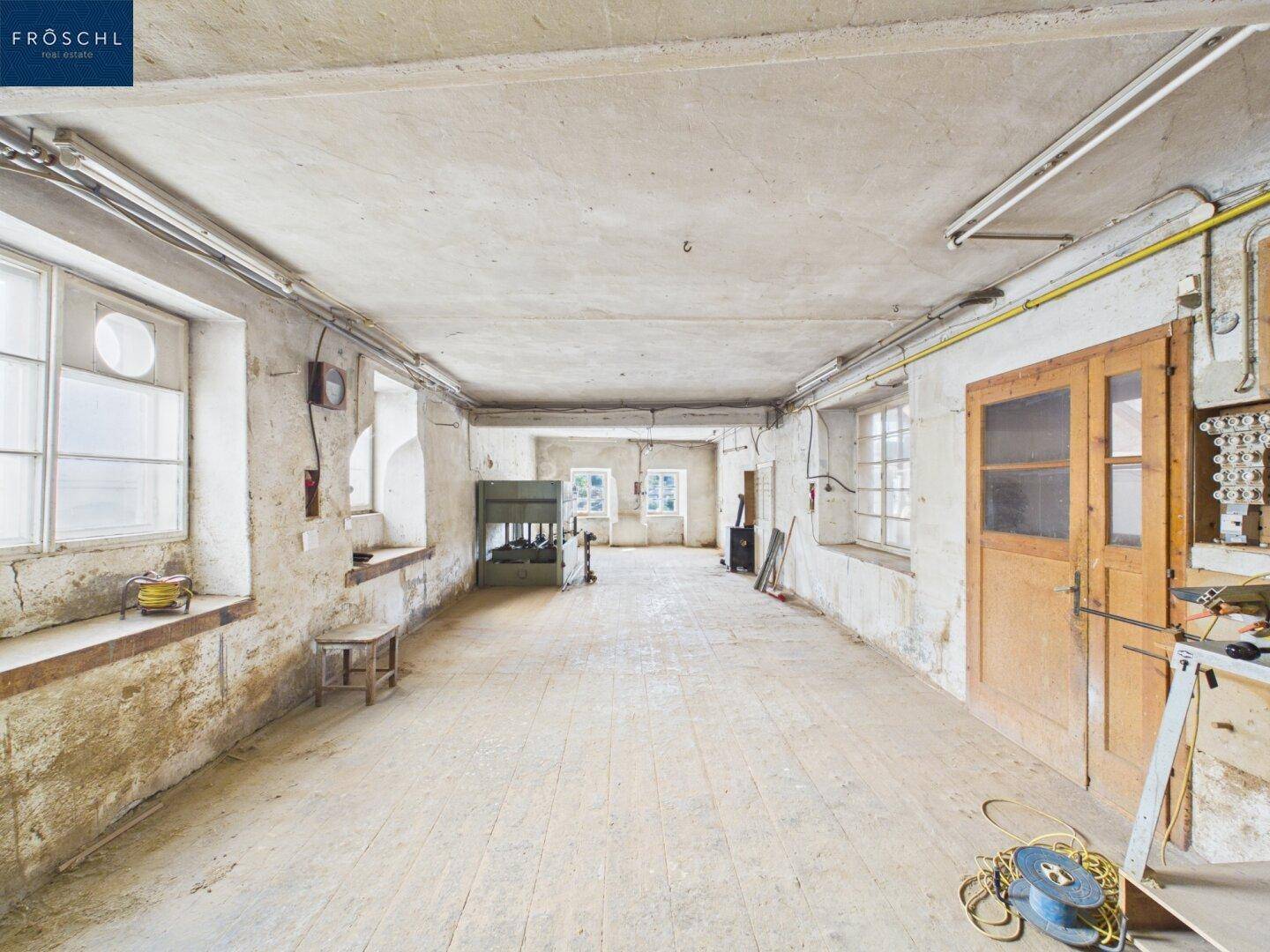 Geräumiger, unfertiger Raum im Untergeschoss mit Holzdielenboden und sichtbaren Installationen.