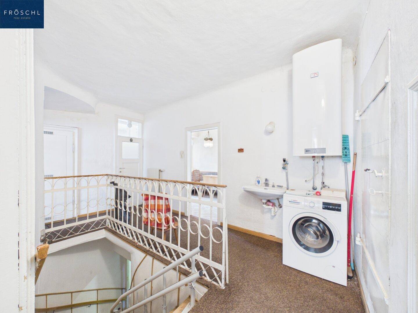 Flur mit Treppenhaus, Waschmaschine und Warmwasserbereiter, der als Hauswirtschaftsraum dient.