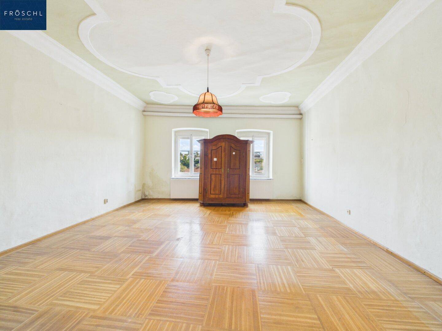 Geräumiges Schlafzimmer mit Fischgrätparkett, einer Stuckdecke und einem antiken Holzschrank.