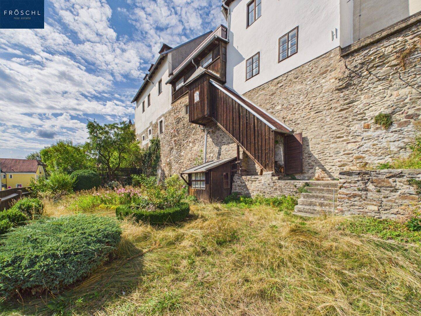 Terrassierter Gartenbereich mit alten Steinmauern, Treppen und einem historischen Gebäude im Hintergrund.