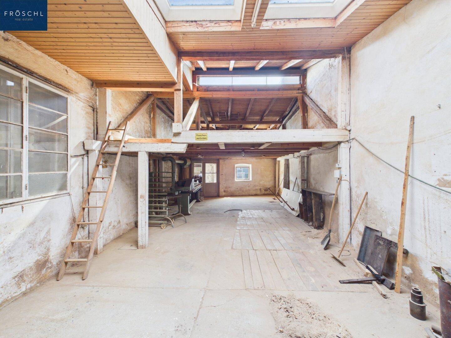 Dachboden mit sichtbaren Holzbalken, Dachfenstern und einer Holzleiter zu einer oberen Ebene.