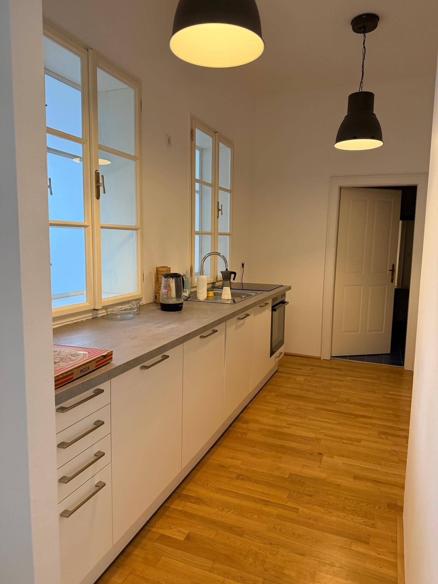 Funktionale Küche mit weißen Unterschränken, Holzfußboden und zwei Fenstern für viel Tageslicht.