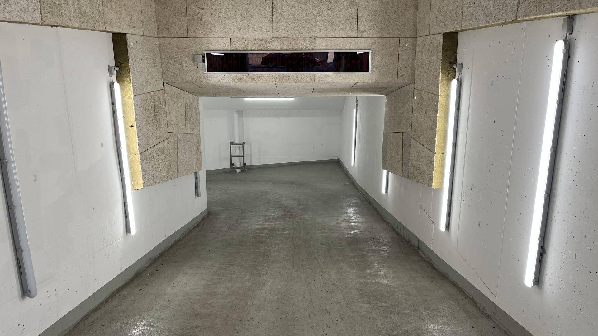 Beleuchtete Rampe führt in die Tiefgarage mit Betonboden und weißen Wänden.