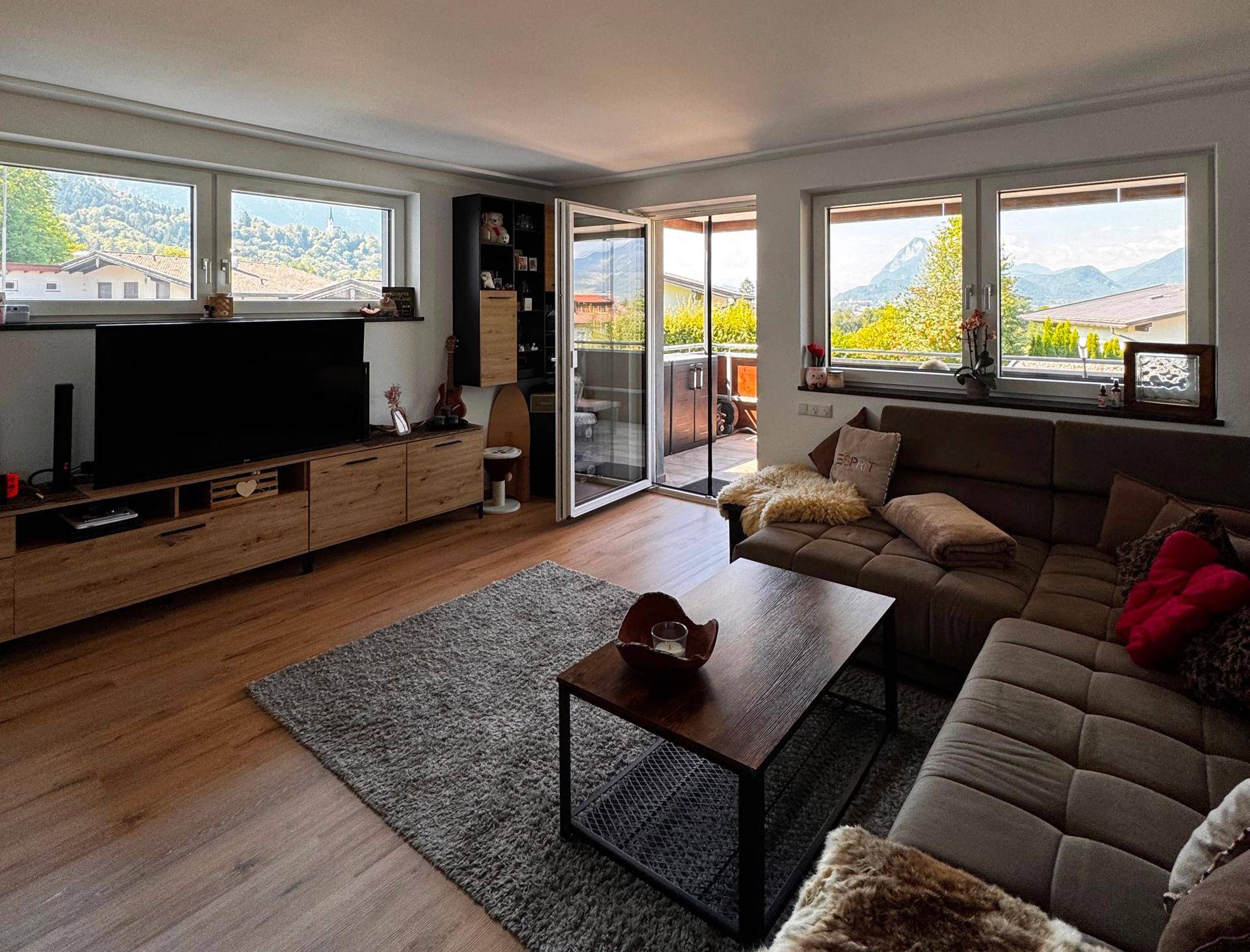 Helles Wohnzimmer mit Holzboden, großem Sofa und Zugang zu einem Balkon mit Bergblick.