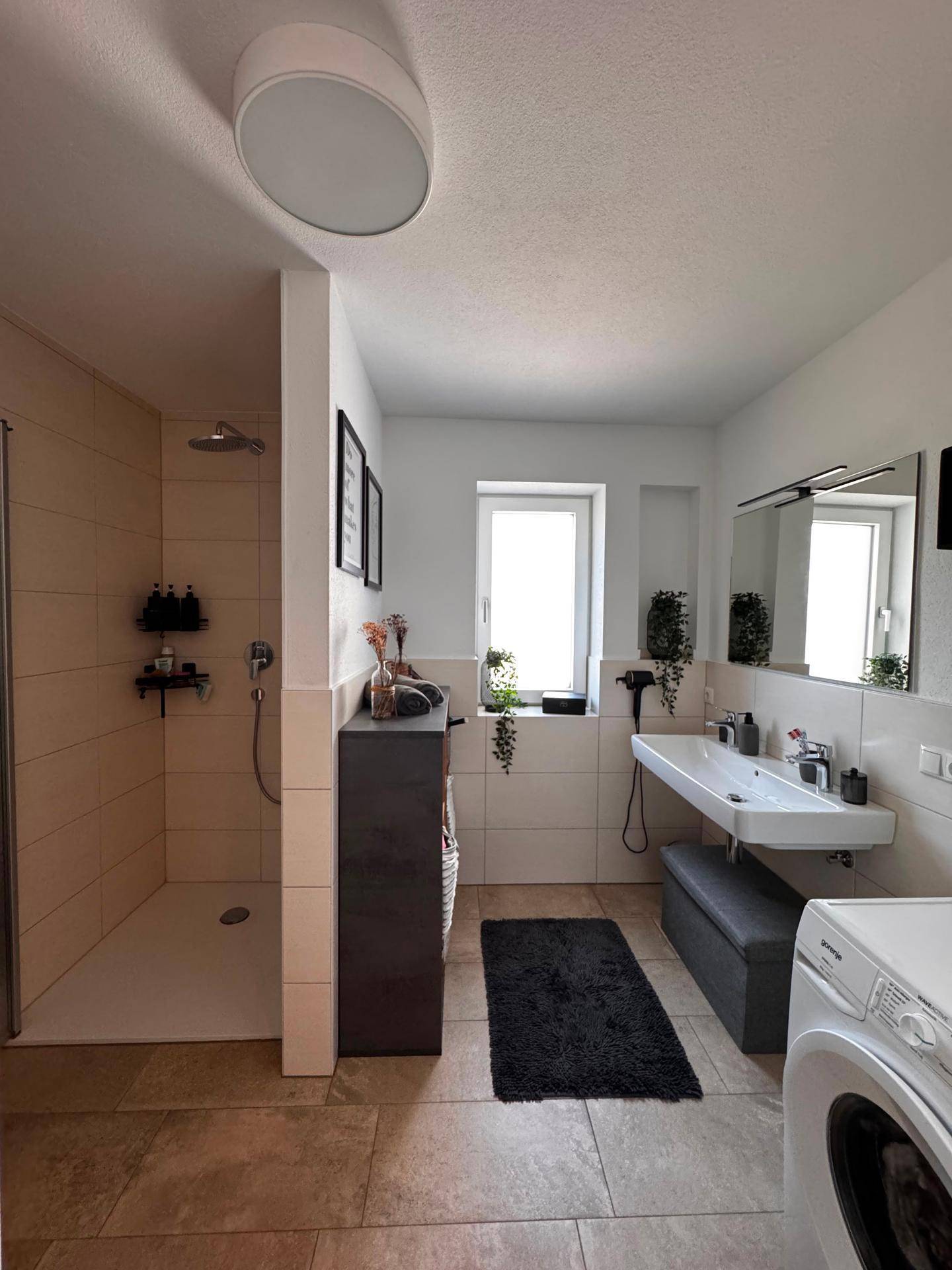 Geräumiges Badezimmer mit ebenerdiger Dusche, Doppelwaschbecken und Waschmaschine.