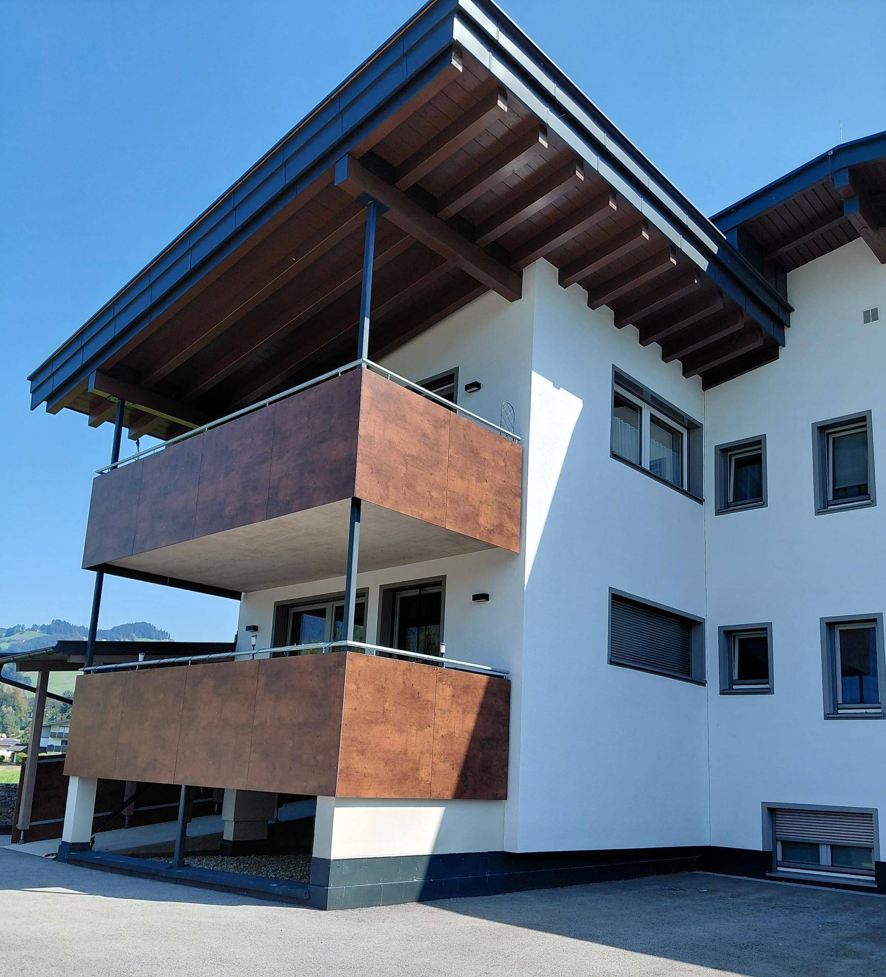 Ansicht des modernen Gebäudes mit Holzdetails an den Balkonen und dem Dachüberstand.