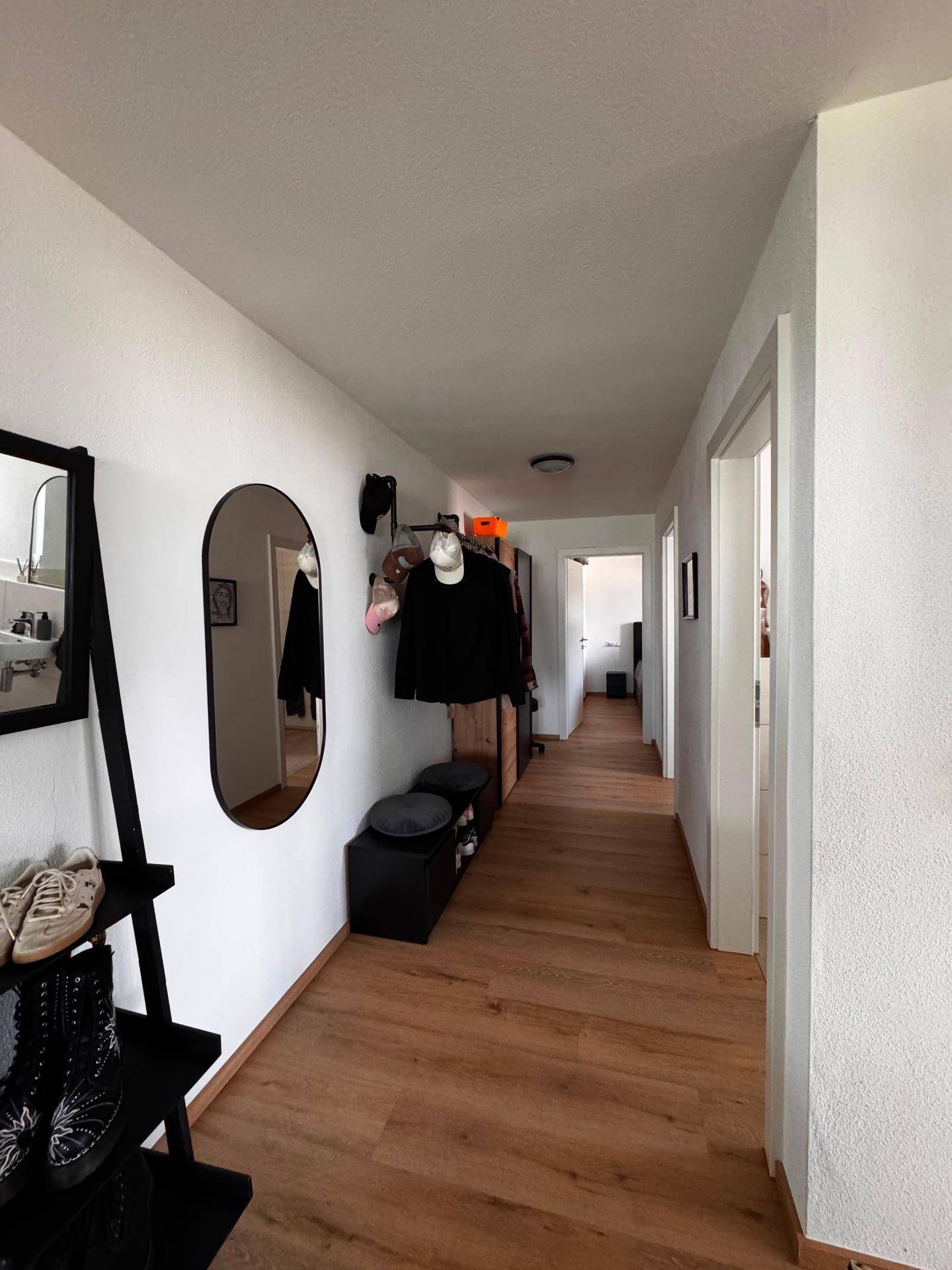 Heller Flur mit Holzboden, Garderobe und Spiegel, der zu weiteren Räumen führt.