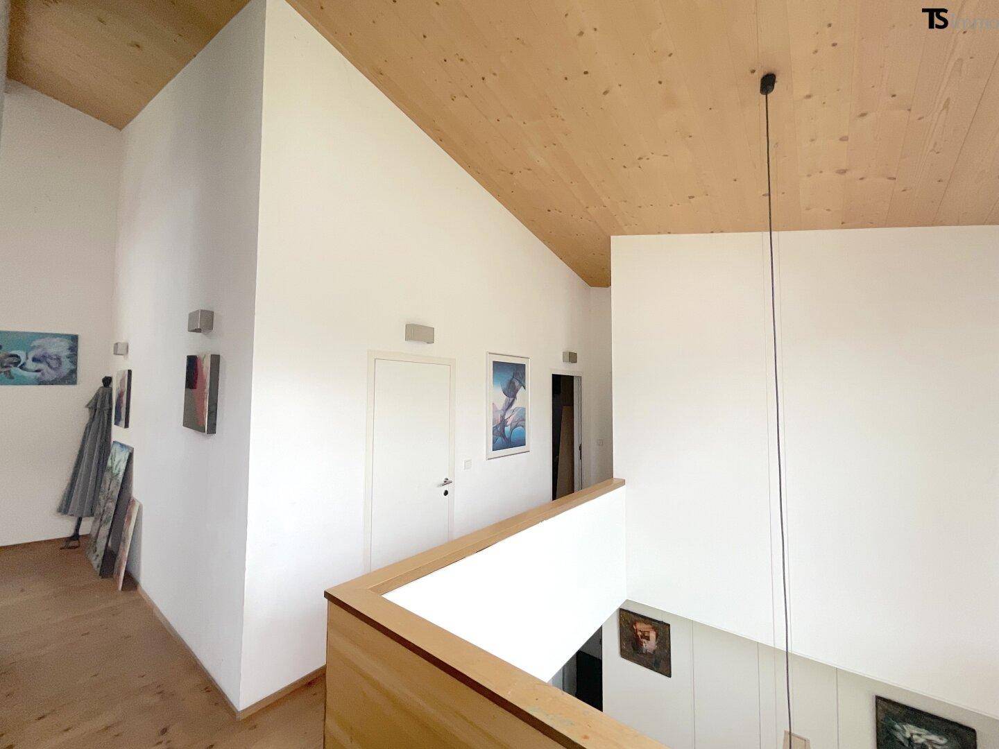 Heller Flur im Obergeschoss mit Holzdecke, weißen Wänden und Blick auf den unteren Bereich.