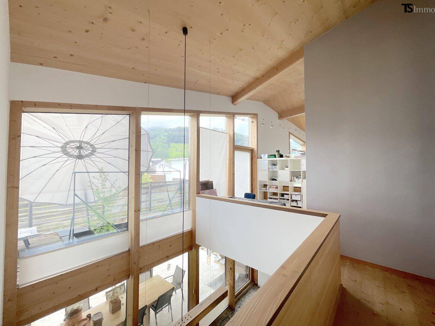 Offene Galerie im Obergeschoss mit Holzdecke und Blick auf den unteren Wohnbereich durch große Fenster.
