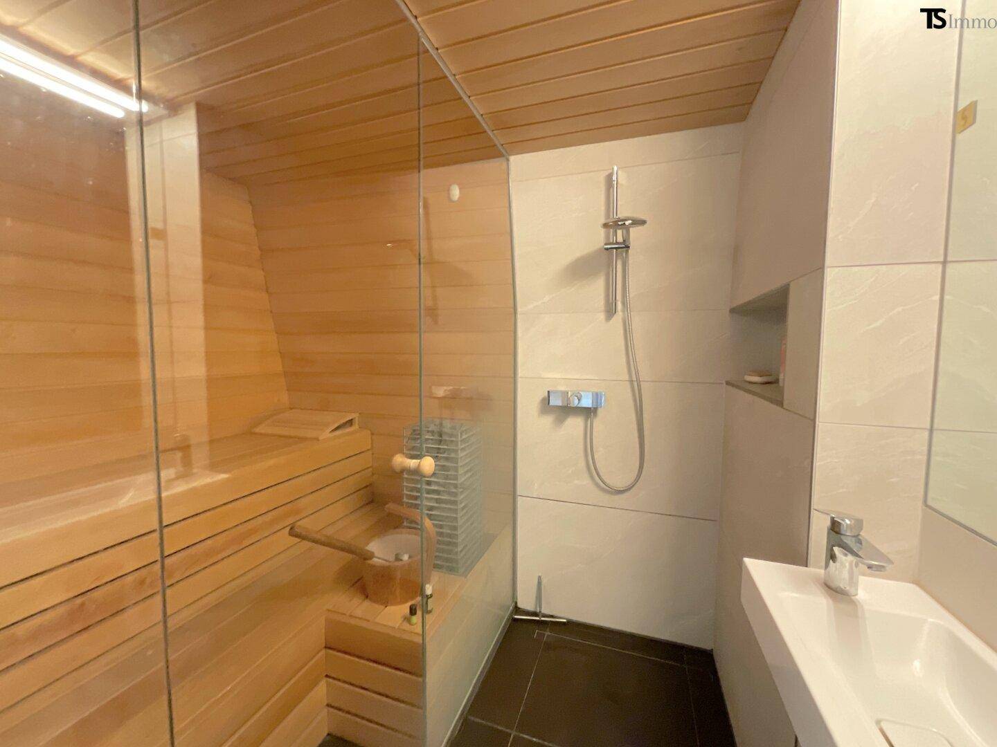 Moderne Sauna mit Holzverkleidung und angrenzendem Duschbereich mit Einzelwaschbecken.