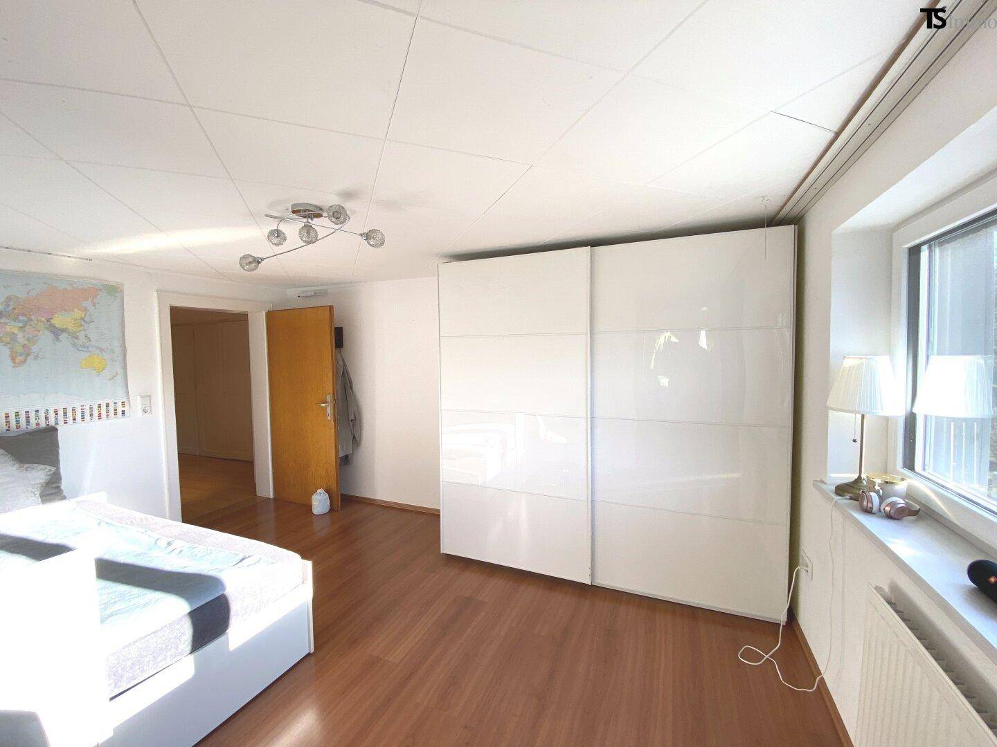 Schlafzimmer mit weißem Schiebetürenschrank, Holzboden und Fenster für viel Tageslicht.