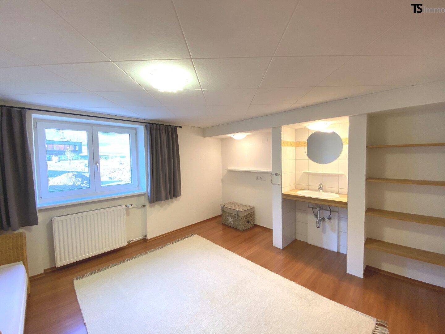 Schlafzimmer mit Holzboden, Fenster und integriertem Waschbeckenbereich.