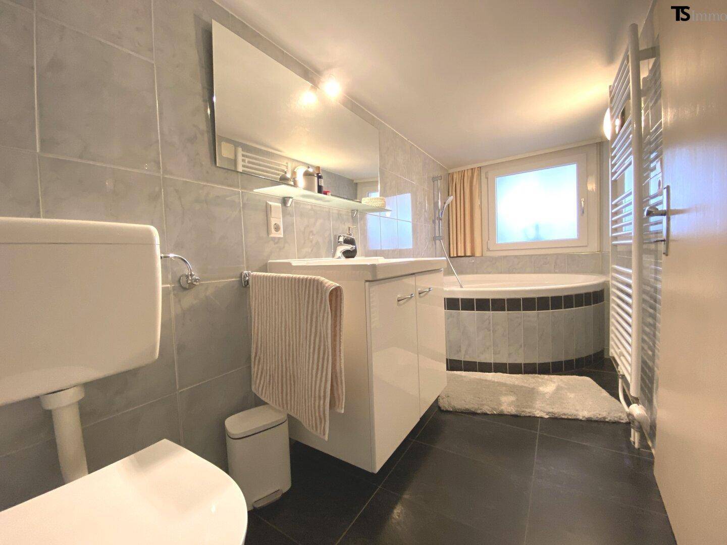 Modernes Badezimmer mit runder Badewanne, Waschtisch und beheiztem Handtuchhalter.